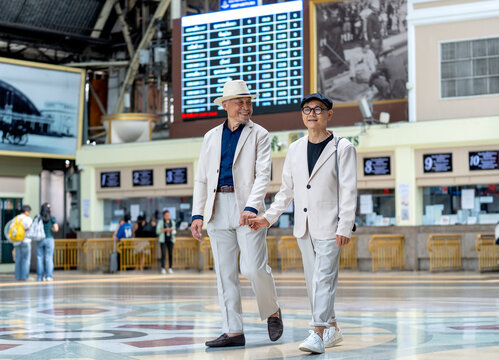 Couple senior lover of lgbt walk together in front of ticket counter of train station with happiness.