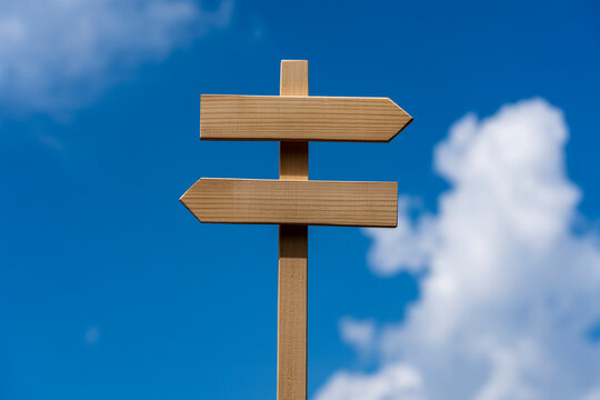 Blank wooden signpost with arrows pointing left and right against bright blue sky, closeup. Concept of making choices, path selection, navigation, future decisions, or strategy template