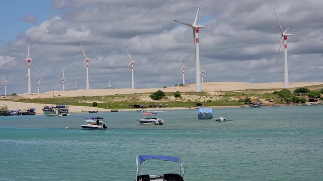 Wind Turbines on Sand Dunes Overlooking Boats in the Turquoise Water, Mundau Beach, Brazil