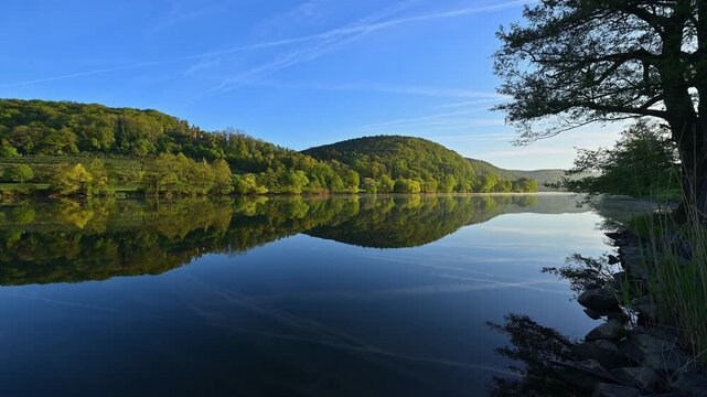 Ein ruhiger Fluss mit Reflexion der bewaldeten H&uuml;gel und des blauen, wolkenlosen Himmels, Freudenberg, Main, Maintal, Baden-W&uuml;rttembergs, Deutschland