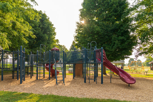 Empty Park playground equipment surrounded by trees in morning light