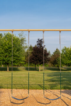 Empty playground swings against clear blue sky in morning light at park