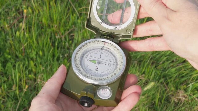 Hiker holds an open compass and uses it to navigate the outdoors during a summer hike. Concepts of travel destinations, sports tourism, hiking