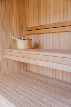 Vertical empty wooden sauna interior with bucket and ladle on bench in spa retreat