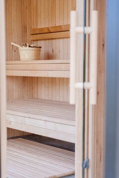 Vertical view through glass door into empty wooden sauna with benches, bucket and ladle