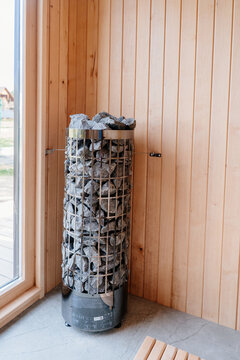 Vertical electric sauna heater filled with stones inside modern wooden wellness room
