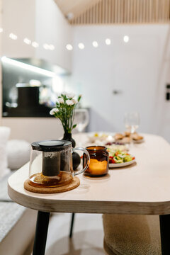 Vertical cozy dinner table with glass teapot, candle and healthy meal in modern cabin interior
