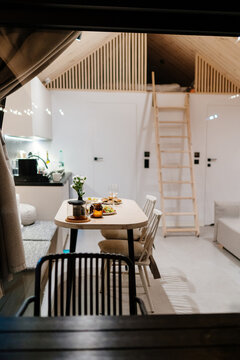 Vertical evening view through window into cozy tiny cabin with dining table and sleeping loft