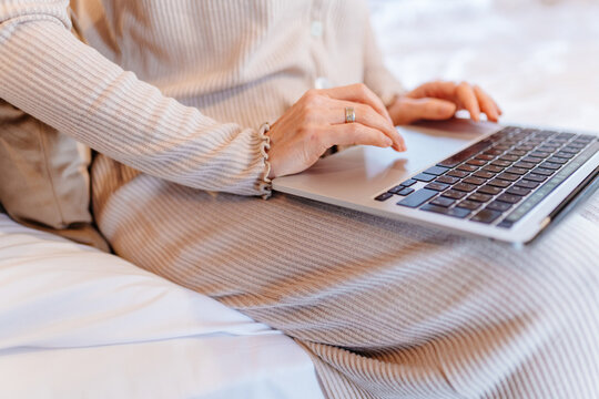 Close-up of mature woman using laptop touchpad while working remotely from comfortable bed