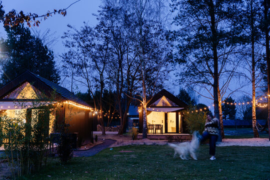 Woman walking with dog between illuminated tiny cabins during tranquil evening nature retreat
