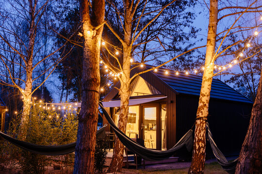 Illuminated tiny cabin surrounded by hammocks and warm garden lights at evening retreat