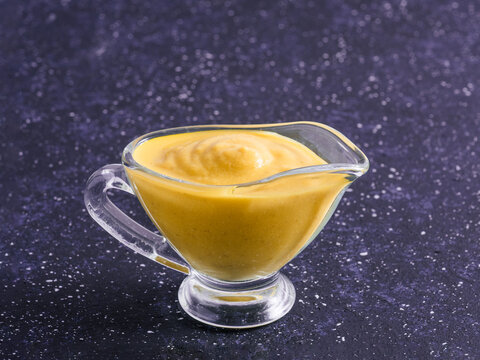 Delicious plant-based dairy-free cheddar cheese sauce with chia seeds served in glass bowl. Vibrant purple background with copy space. Creamy Cheddar sauce with chia seeds on dark background