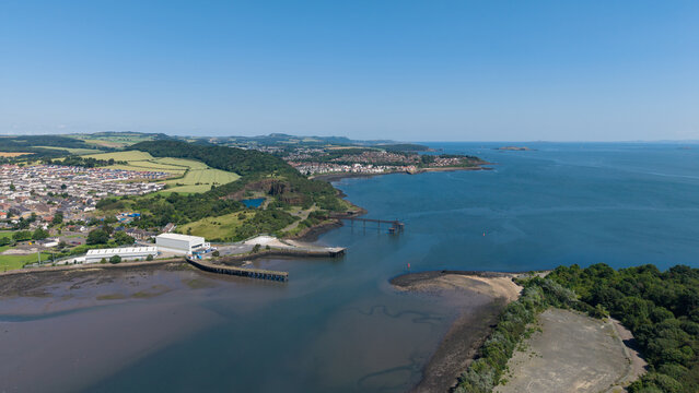Scenic wide angle aerial view of Inverkeithing bay and harbour in Fife, Scotland, showing coastal waters, industrial piers, and the green seaside landscape under a clear blue sky
