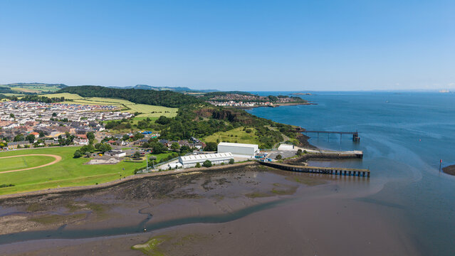 Aerial view of Inverkeithing in Fife, Scotland, showing the coastal village, muddy bay at low tide, industrial piers, and the blue sea waters under a clear summer sky