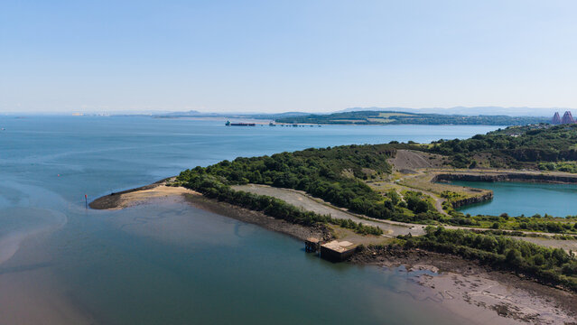 Aerial view of the rocky coastline in Inverkeithing, Fife, showing the sea bay, green shore of Prestonhill Quarry, and coastal waters under a clear blue sky in Scotland
