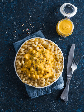 Delicious plant-based pasta dish with homemade dairy-free chia cheddar cheese sauce. Pasta with vegan creamy chia cheddar sauce on dark blue background. Vertical. Copy space