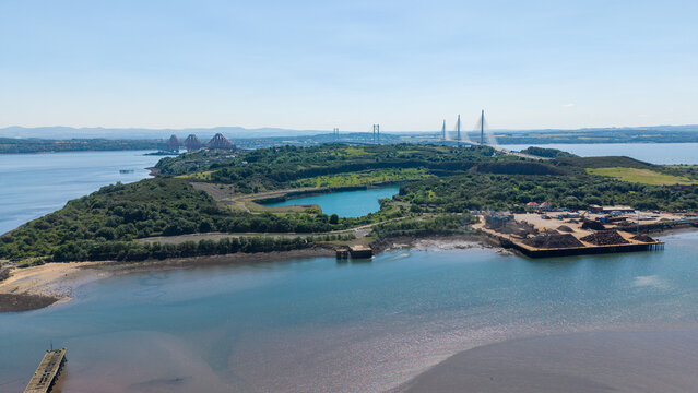 Aerial drone view of Prestonhill Quarry filled with blue water in Inverkeithing, Fife, with the three Forth bridges spanning the estuary in the background under a clear sky