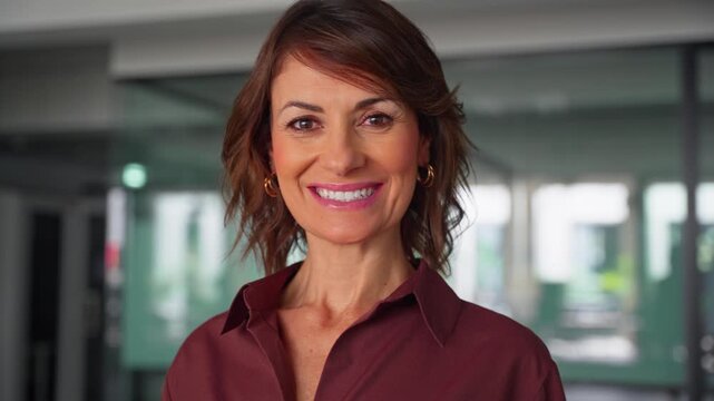 Close up portrait of happy latin businesswoman looking at camera in office. Smiling mature woman shows beautiful face with toothy smile. Cheerful female business executive enjoys career at work.