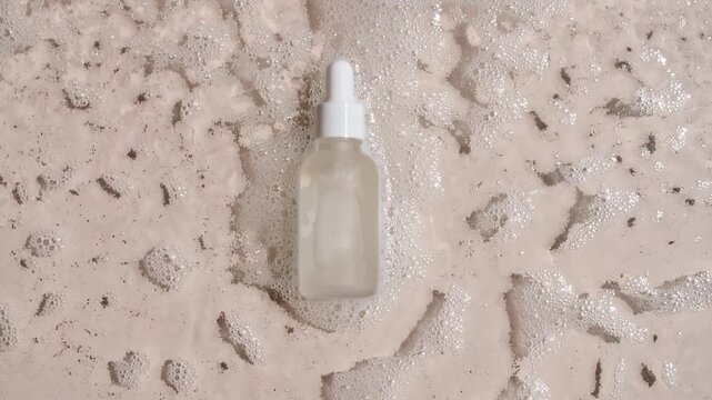 Bottle with a pipette for collagen serum, oil, toner on water texture background surface with bubbles of white soapy foam. Medical skin care. Packaging for design, advertising of a cosmetic product.4k