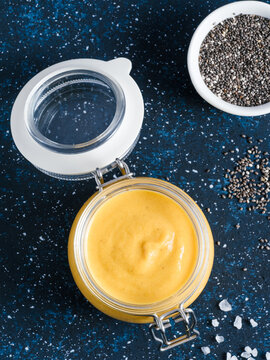 Homemade plant-based chia cheeze sauce for snacks, tacos and nachos. Creamy dairy-free dip on dark background with copy space. Vertical. Creamy Cheddar sauce with chia seeds on dark blue background
