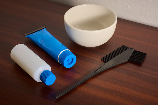 hair dye kit on wooden table top, blue color tube with developer bottle, bowl and tint brush with copy space, salon hair coloring treatment