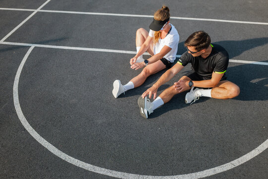Couple stretches together on a sunny day at the basketball court, preparing for an afternoon of fitness and fun