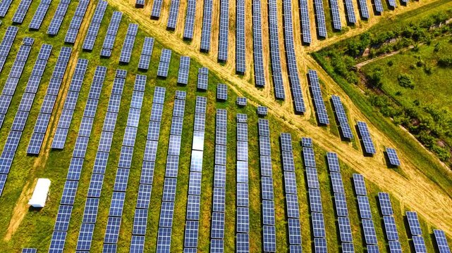 Top down view of solar panel rows on grass. Symmetric photovoltaic grid on green lawn, white container, aerial photography, bright daytime lighting.