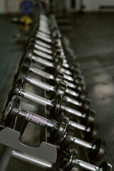 Fototapeta premium Vertical shot of dumbbells lining gym rack, supporting strength training, fitness routine, muscle building concept. Ideal for workout promotion, wellness branding, sports ads