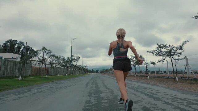Back view of braided woman running along tree lined countryside road