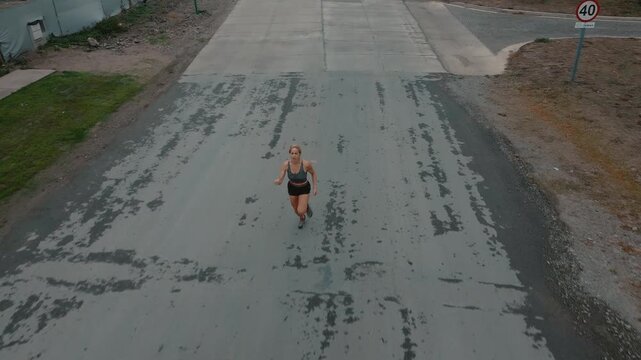 Aerial front view of female runner approaching sidewalk beside wooden fence