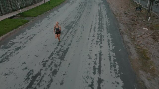 Overhead shot of female runner crossing wide open road bordered by grass