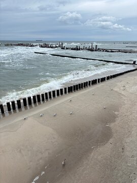Calm beach with waves and wooden pier under cloudy sky  