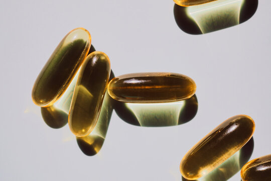 Yellow omega-3 capsules with transparent oil casting shadows on light surface