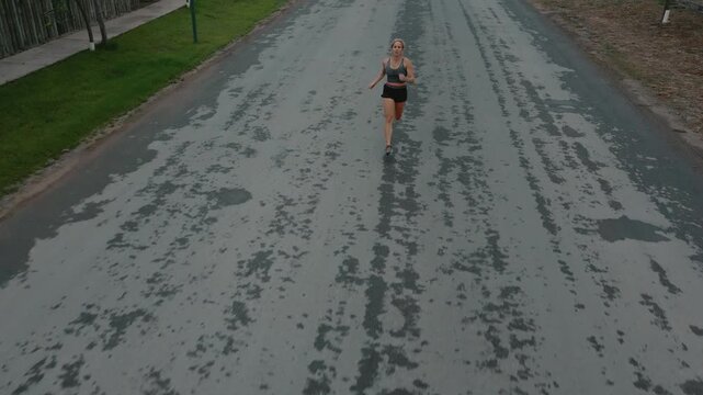 Aerial shot of female runner heading toward camera beside fence and grass