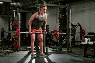 Fototapeta premium Young adult Caucasian man lifting barbell in gym, training strength and endurance for fitness goals. Wide shot, useful for workout programs, personal training, sports marketing