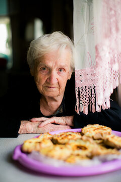 Elderly woman looking at the camera from a kitchen table with homemade pastries in the foreground creating a warm portrait of home life