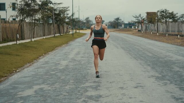 Female athlete sprinting down straight roadway past trees and buildings