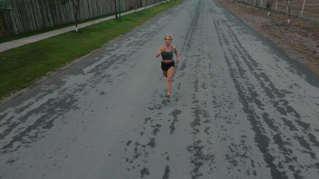 Drone shot of female runner passing steadily along road lined with fence