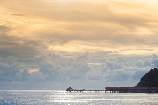 Water chalets and a long pier stretch into the sea under sunset clouds at Burau Bay, Langkawi, Malaysia