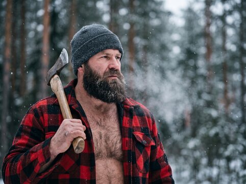 Woodsman's Resolve: A rugged, bearded woodsman, topless in a red flannel shirt and beanie, carries an axe over his shoulder, his breath misting in the cold, snowy forest.