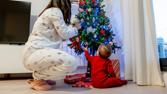 Family decorating Christmas tree with baby in pajamas