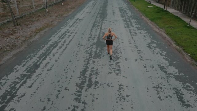 High angle shot of female runner along tree lined path bordered by grass