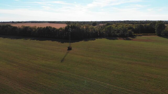 Horizontal 4K 24fps aerial drone video flying over flat agricultural fields in Friuli, Italy, during autumn. The shot reveals a winding stream next to a dirt path, a line of trees, and an electricity 
