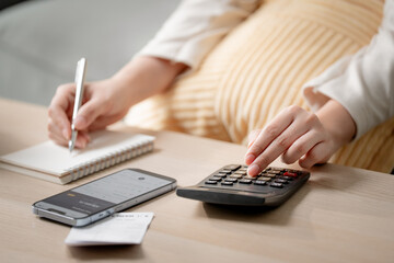 Fototapeta premium Personal budgeting concept. Anonymous person calculating household expenses with calculator while writing notes beside smartphone at home. Budget, finance, savings, planning, expenses