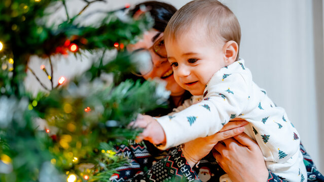 Baby reaching for Christmas tree lights with mom