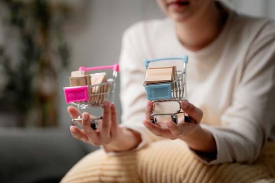 Online shopping comparison concept. Anonymous person comparing miniature shopping carts with parcels to choose the best online store. Shopping, ecommerce, comparison, retail, choice