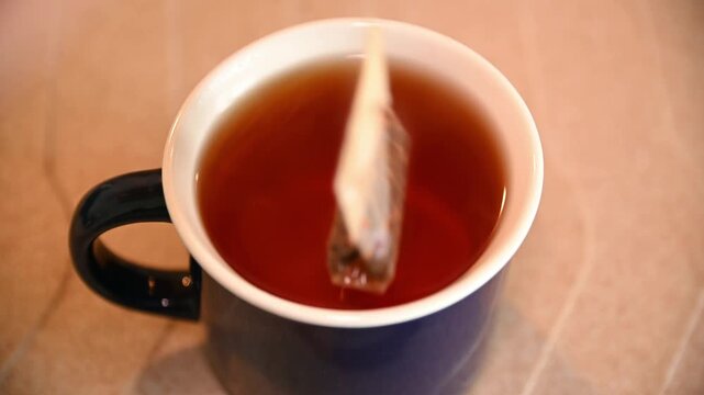 Tea bag steeping and stirring in ceramic mug on kitchen counter