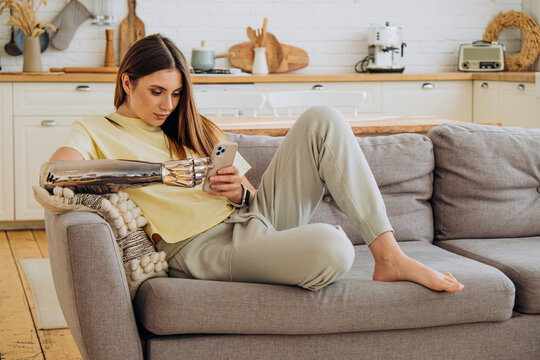 Woman with a bionic prosthetic arm relaxing on a sofa, browsing smartphone, highlighting technological integration and comfort in domestic settings with assistive devices