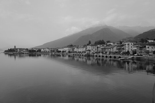Village en bord du lac de C&ocirc;me avec montagne embrum&eacute;e et reflets sur l&rsquo;eau en noir et blanc