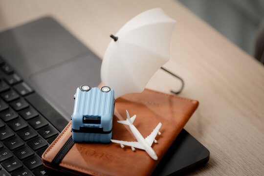 Travel insurance concept. Close-up of a hand protecting travel essentials with an umbrella beside a laptop, symbolizing trip coverage, Travel, insurance, protection, security, vacation